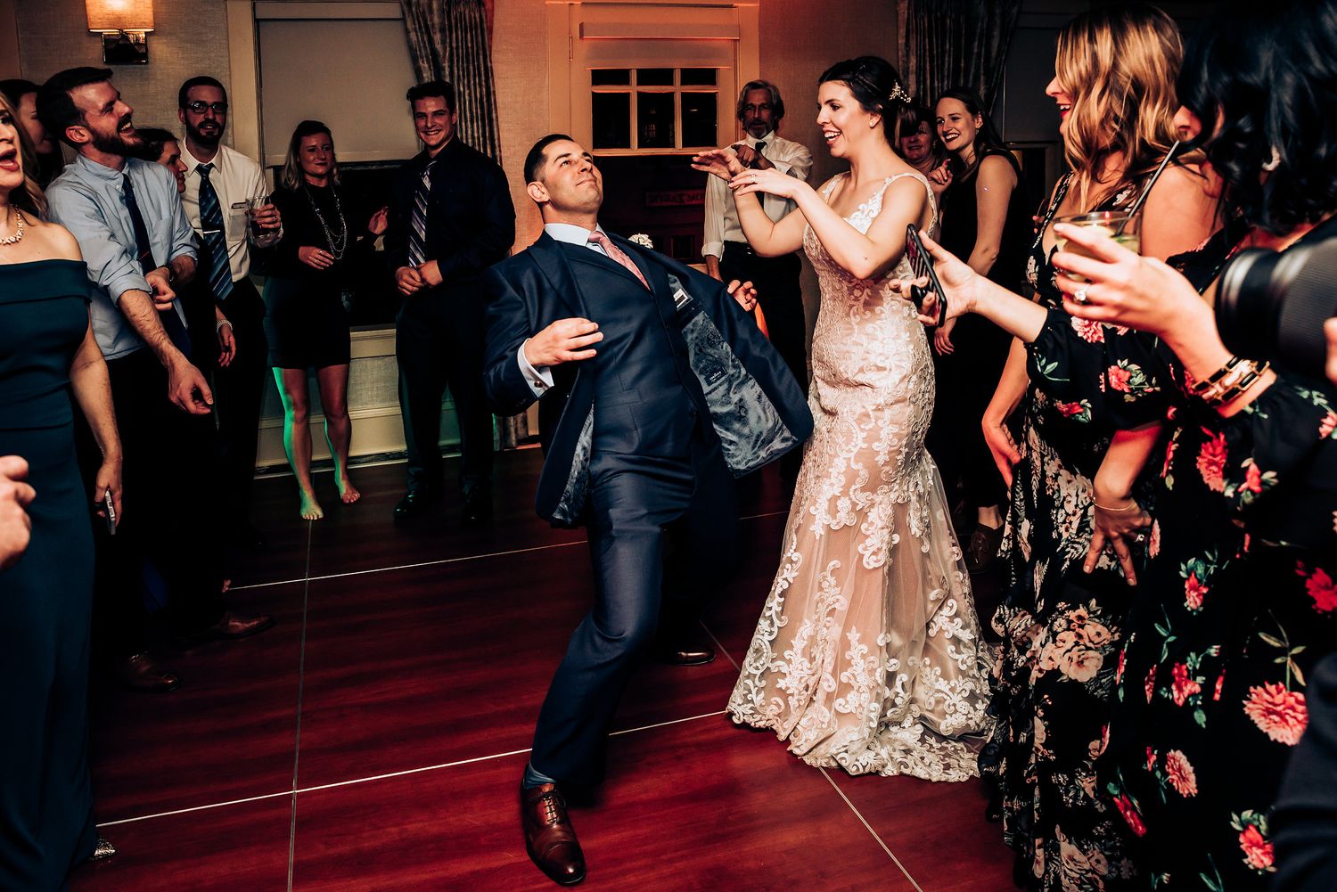 Wedding celebration with dancers enjoying themselves on a dark wooden dance floor.