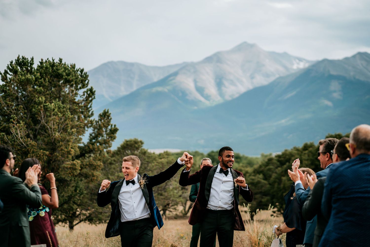 A joyous wedding celebration with the wedding party cheering against a mountainous landscape.