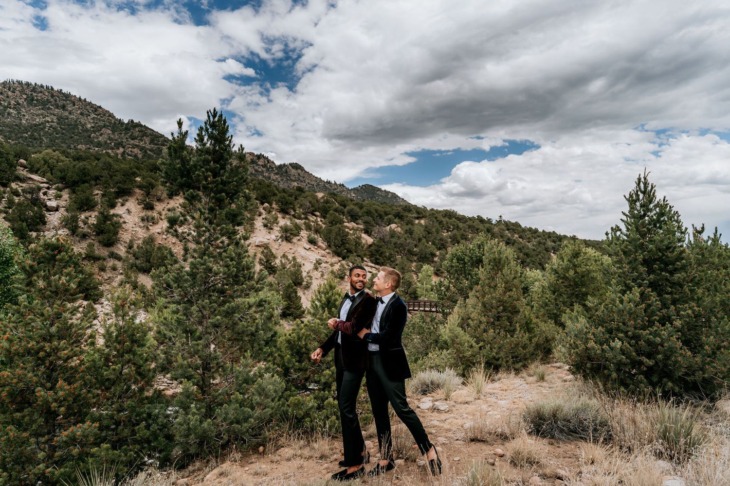 Wedding couple embracing on hillside with mountain landscape behind them.
