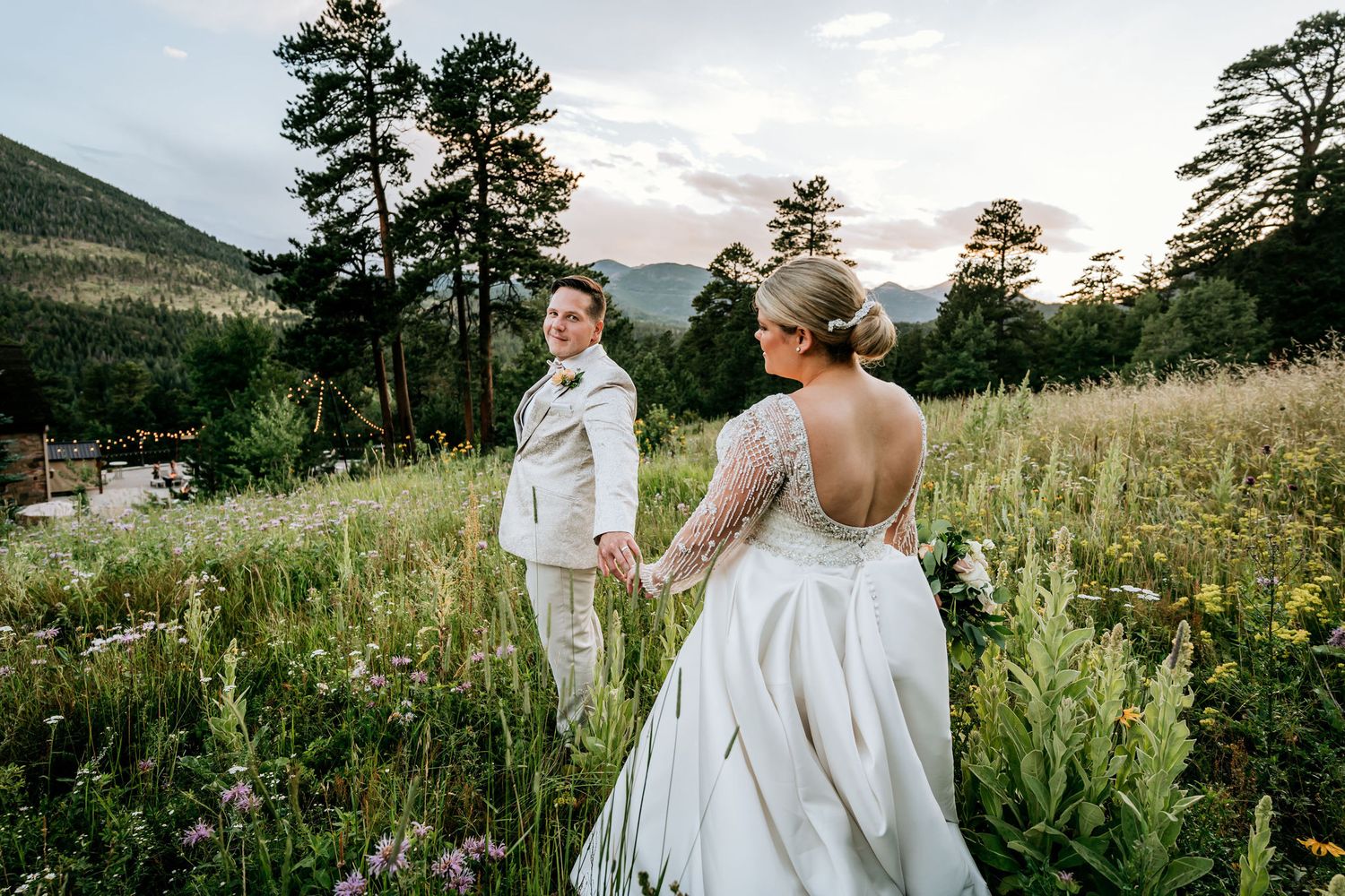 Wedding couple holding hands while walking through a mountain meadow at sunset.