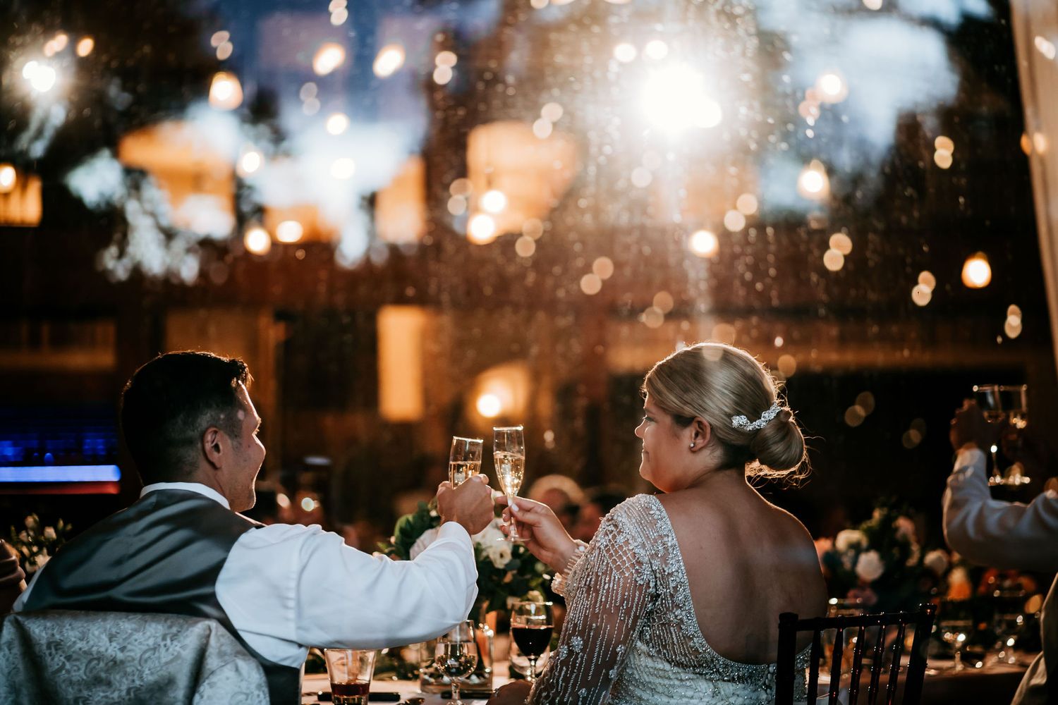 Couple toasting champagne glasses at their wedding reception under sparkly lights.