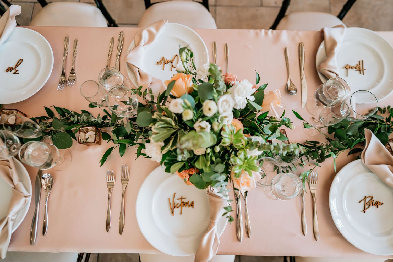 Elegant table setting with floral centerpiece, white plates, and blush pink linens.