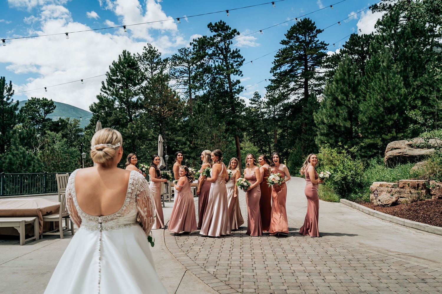 A bride and her bridesmaids in pink dresses celebrate outdoors under a bright blue sky.