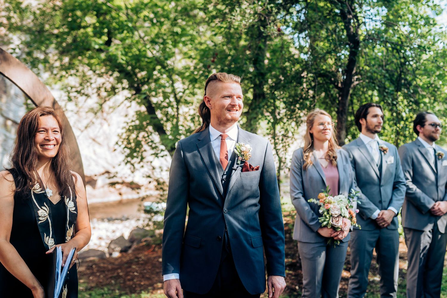 Wedding party members share joyful moment during outdoor ceremony in formal blue suits.