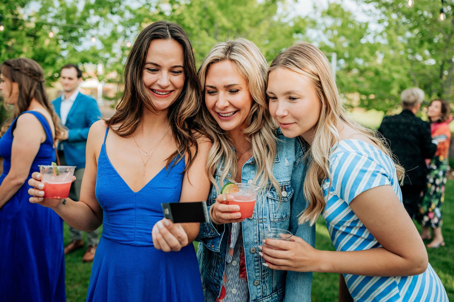 Three people enjoying drinks and laughing together at an outdoor celebration.