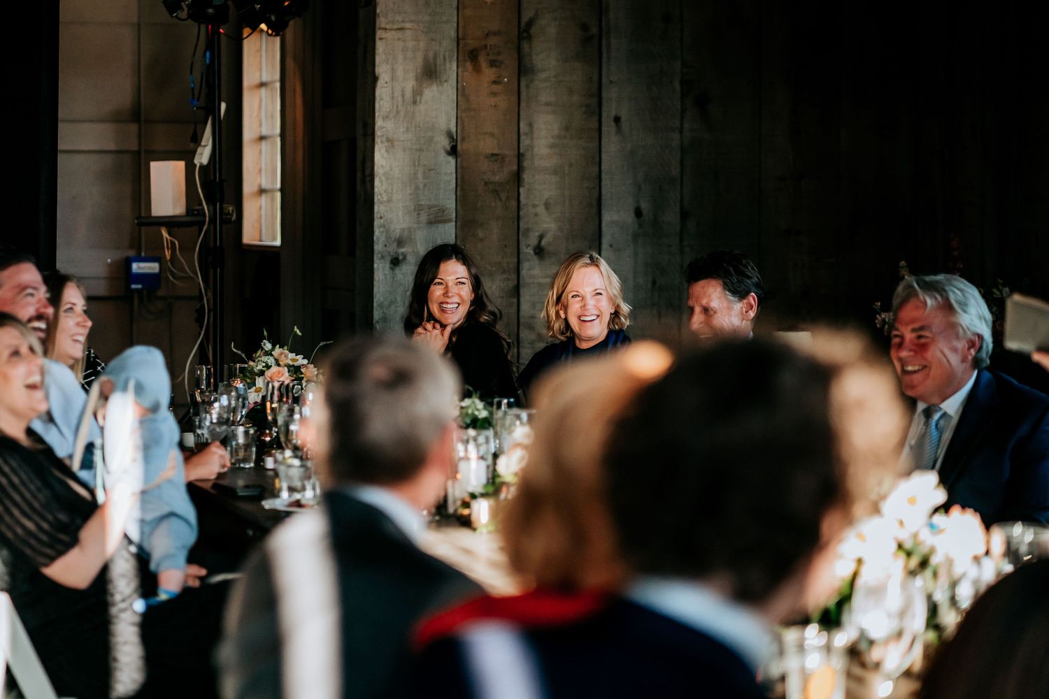 Wedding guests laugh and smile during dinner reception in an industrial-style venue.