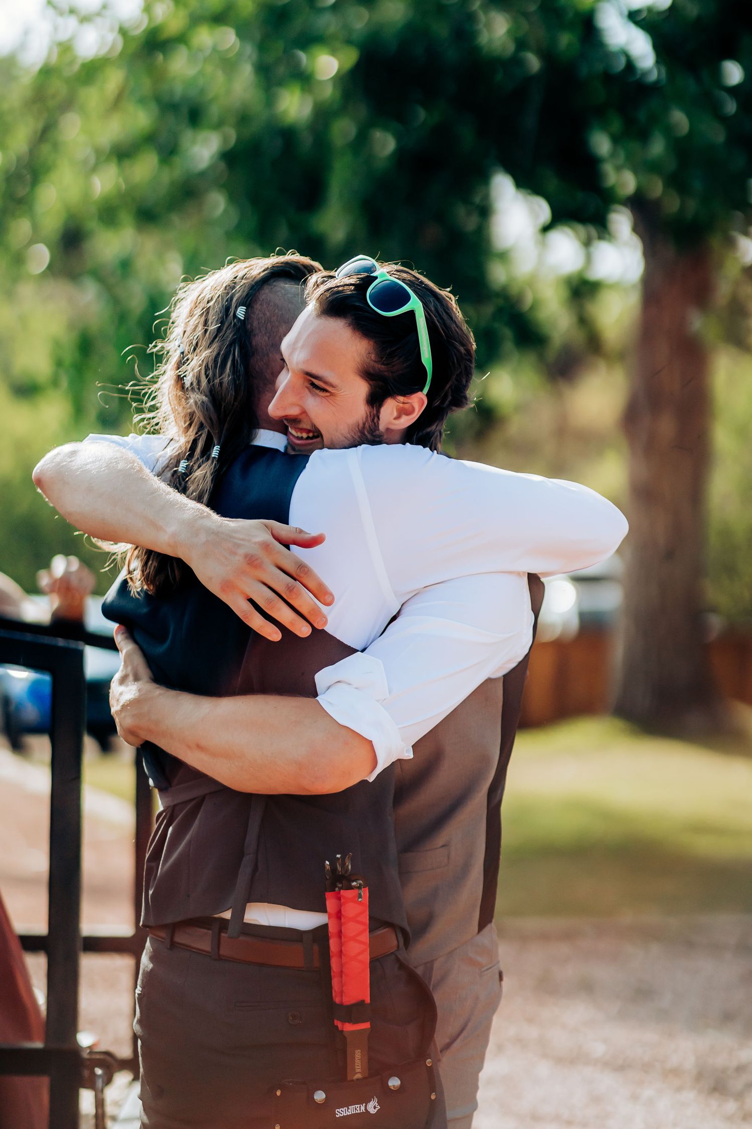 Emotional embrace shared during outdoor celebration with sunlit trees in background.