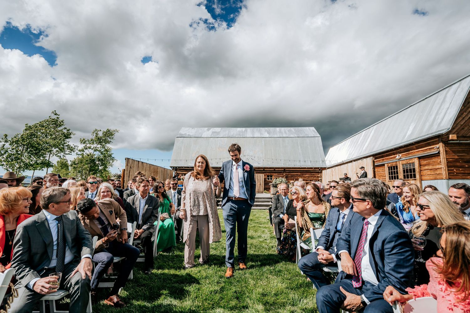 Outdoor wedding ceremony with guests seated in rows at a rustic barn venue.