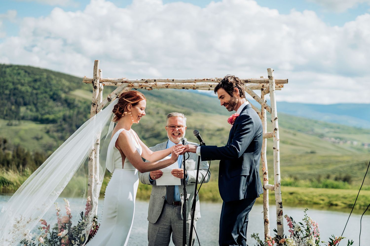 Wedding ceremony at rustic mountain venue with birch arch and scenic valley views in background.