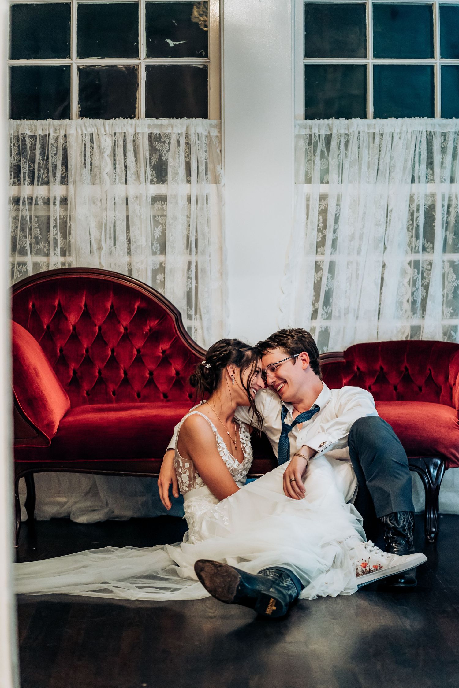 Couple relaxes on a red tufted vintage couch in an elegant white room.