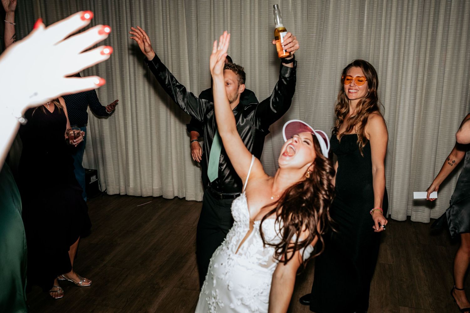 Bride wearing a visor dancing energetically with guests at a fun wedding reception.