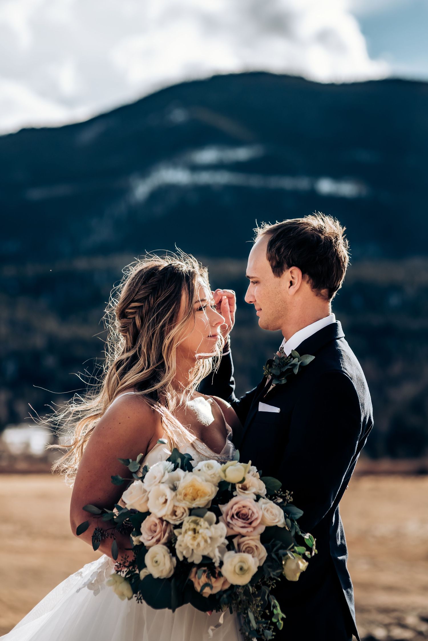 Romantic couple with bouquet sharing intimate moment against mountain backdrop.