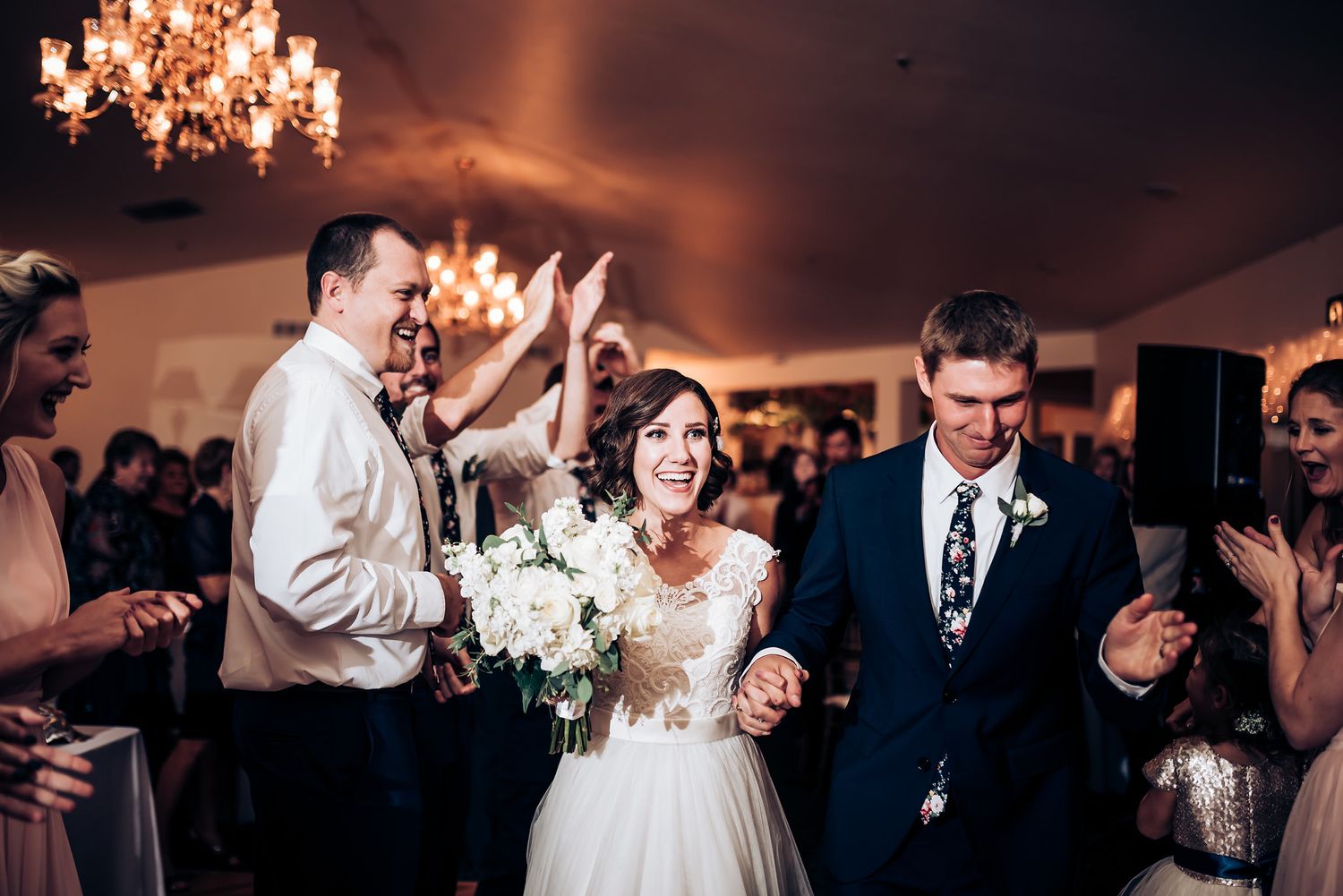Wedding guests celebrating on the dance floor under elegant chandeliers.