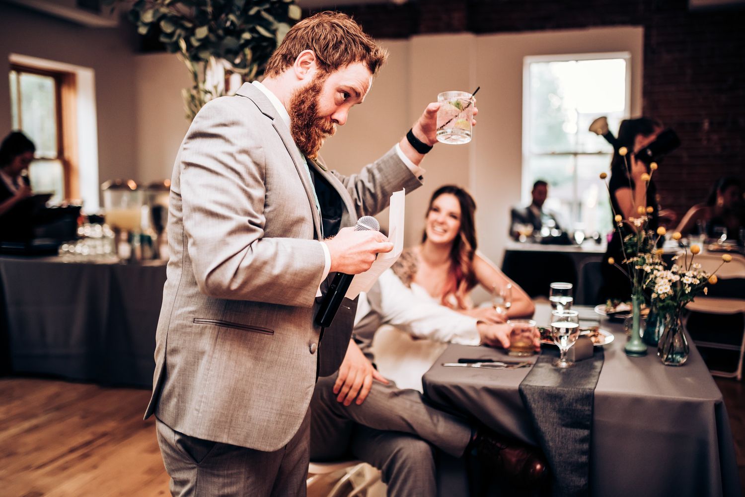 Guest giving an animated speech at wedding reception while others look on.