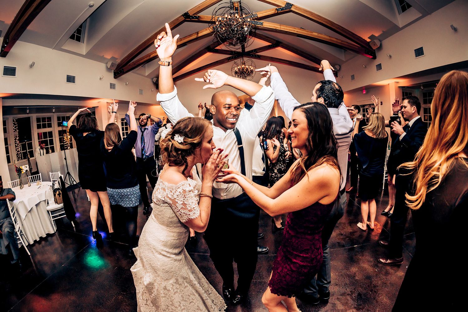 Wedding guests dancing and celebrating together on a dance floor in a venue with exposed wooden beams.