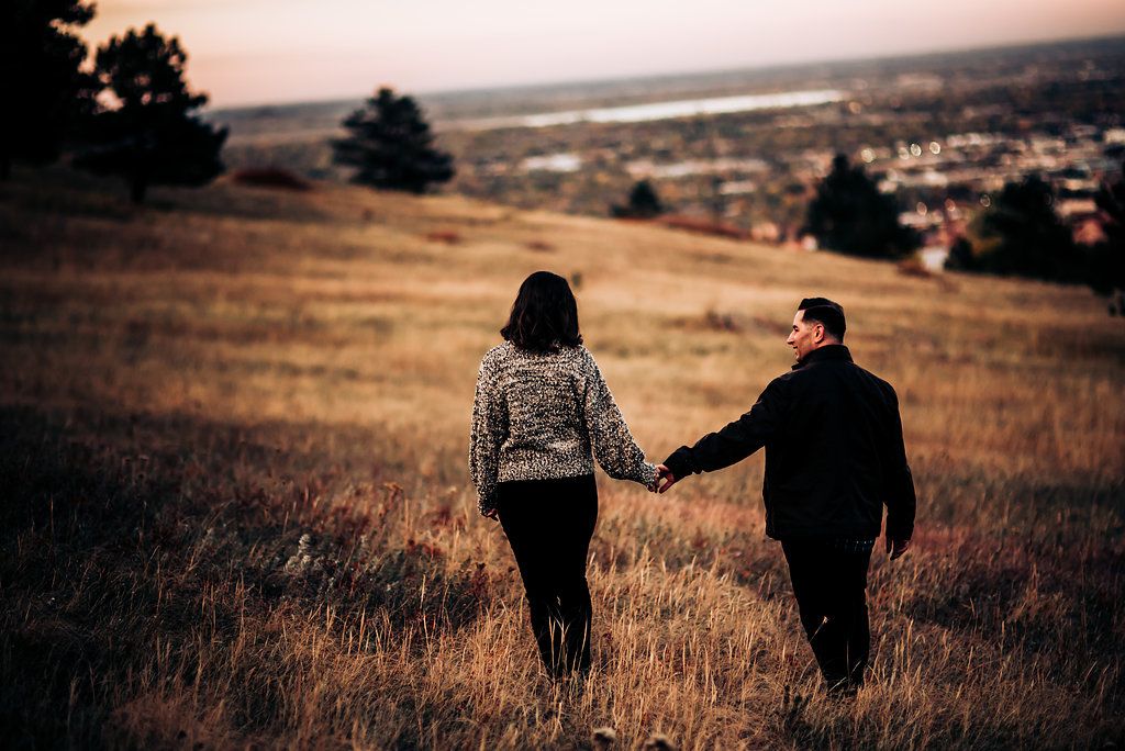Silhouette of couple walking hand in hand through golden grass on hilltop at sunset.