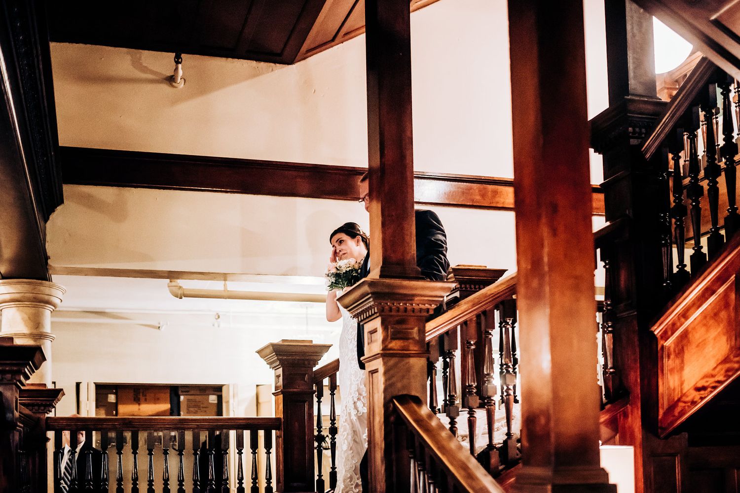 A figure stands alone on a beautiful wooden staircase with ornate railings and architectural details.