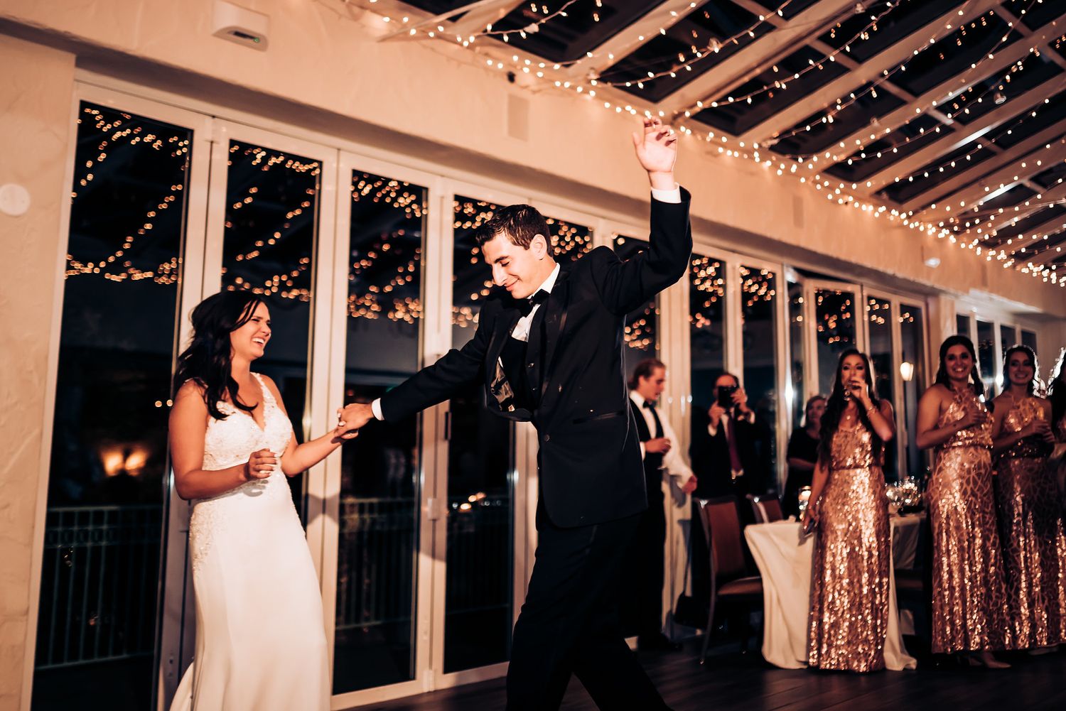 Newlyweds perform playful dance moves during reception with bridesmaids in background.