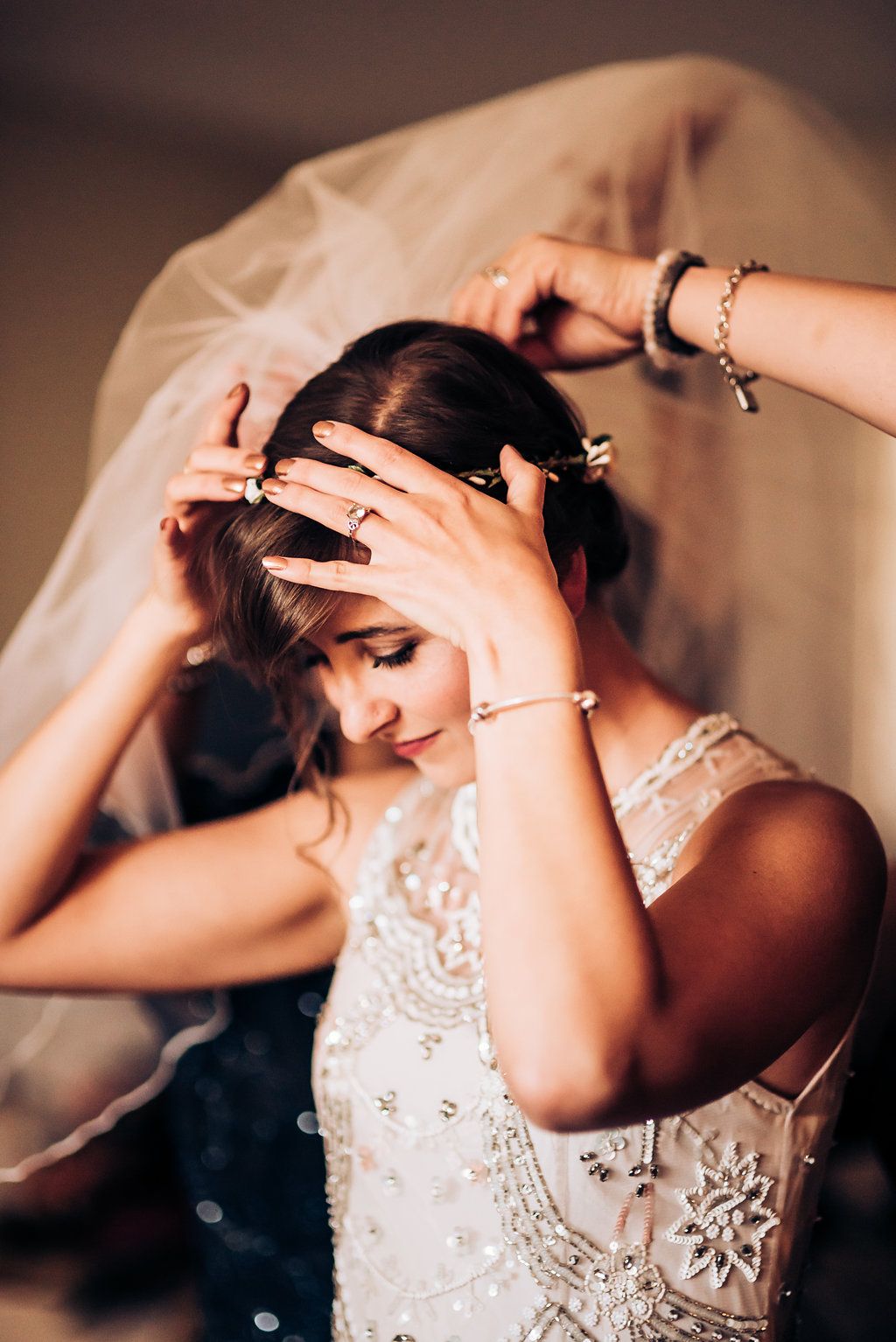 Final touches being made to wedding day hair preparation with veil and beaded dress visible.