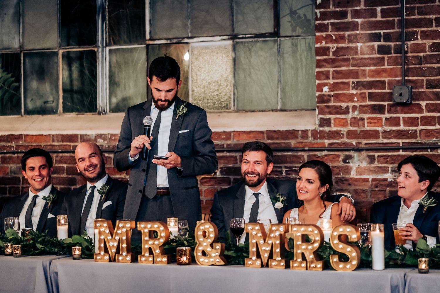 Wedding reception head table with illuminated Mr & Mrs sign during speeches.