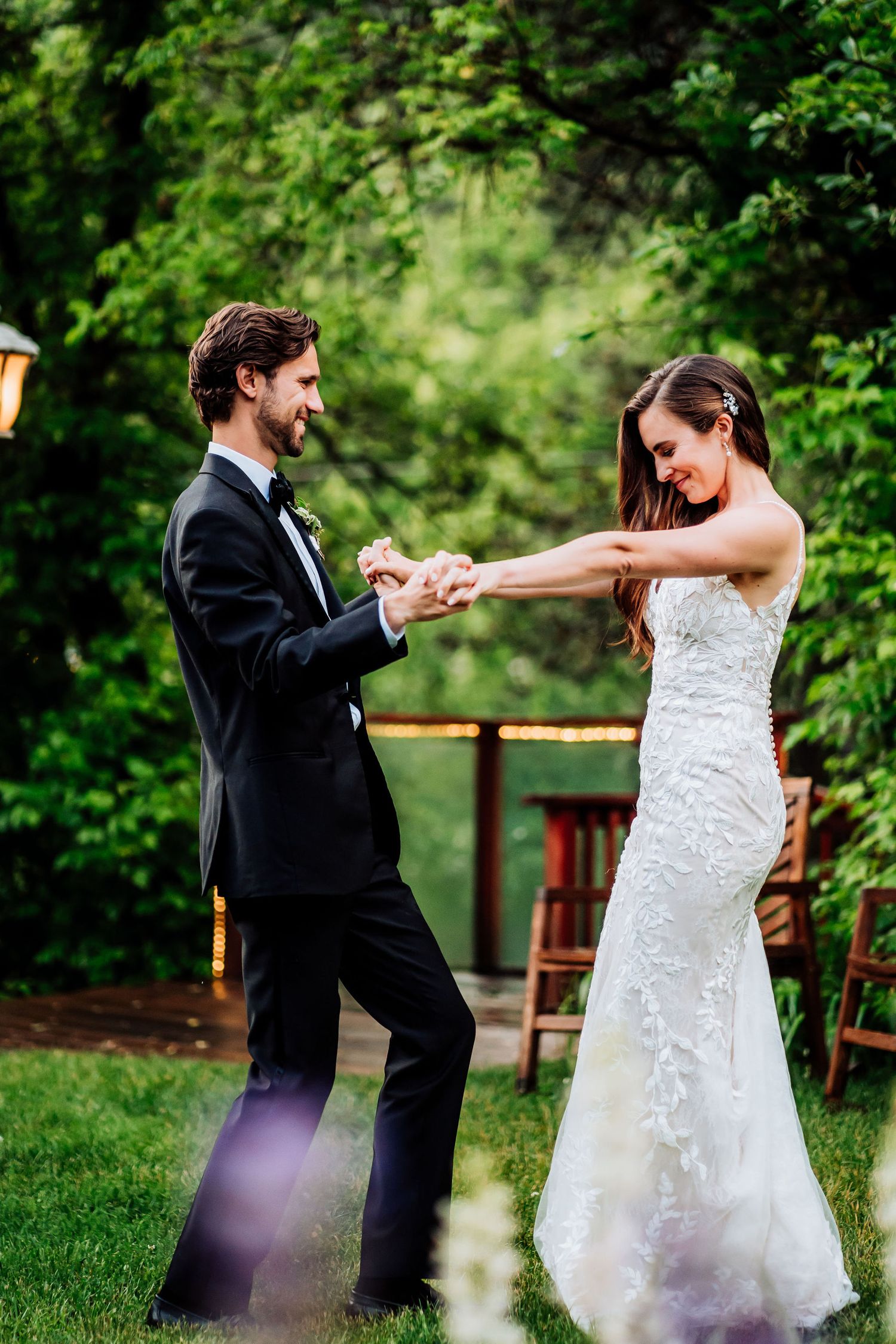 A newlywed couple dances joyfully on their wedding day in a garden setting.