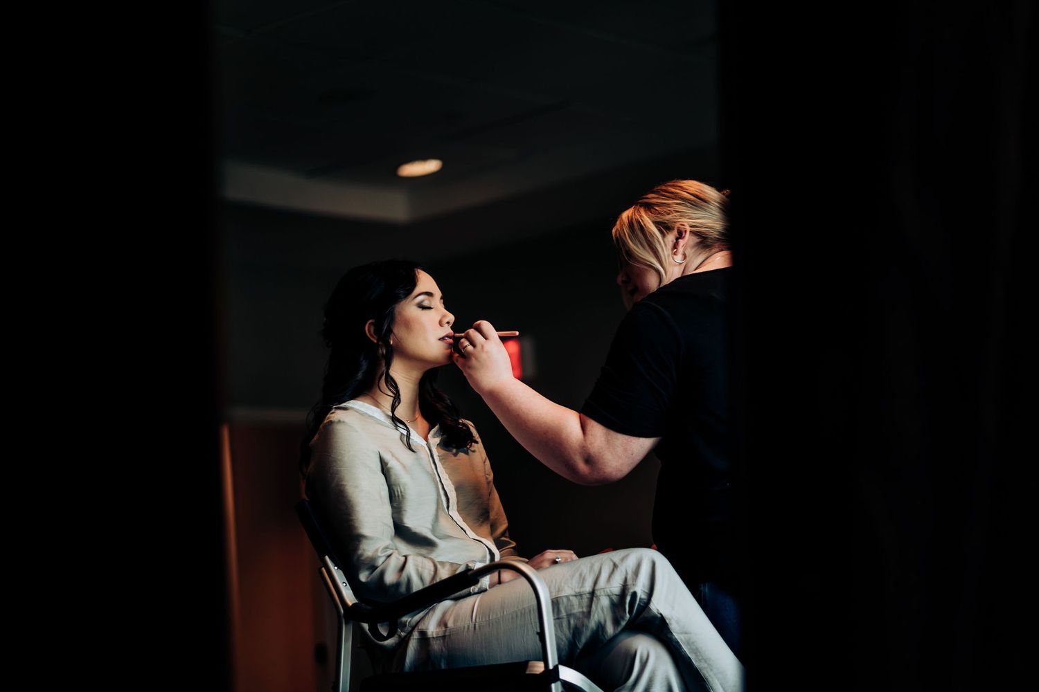 Professional makeup artist working on bridal preparation in moody dramatic lighting.