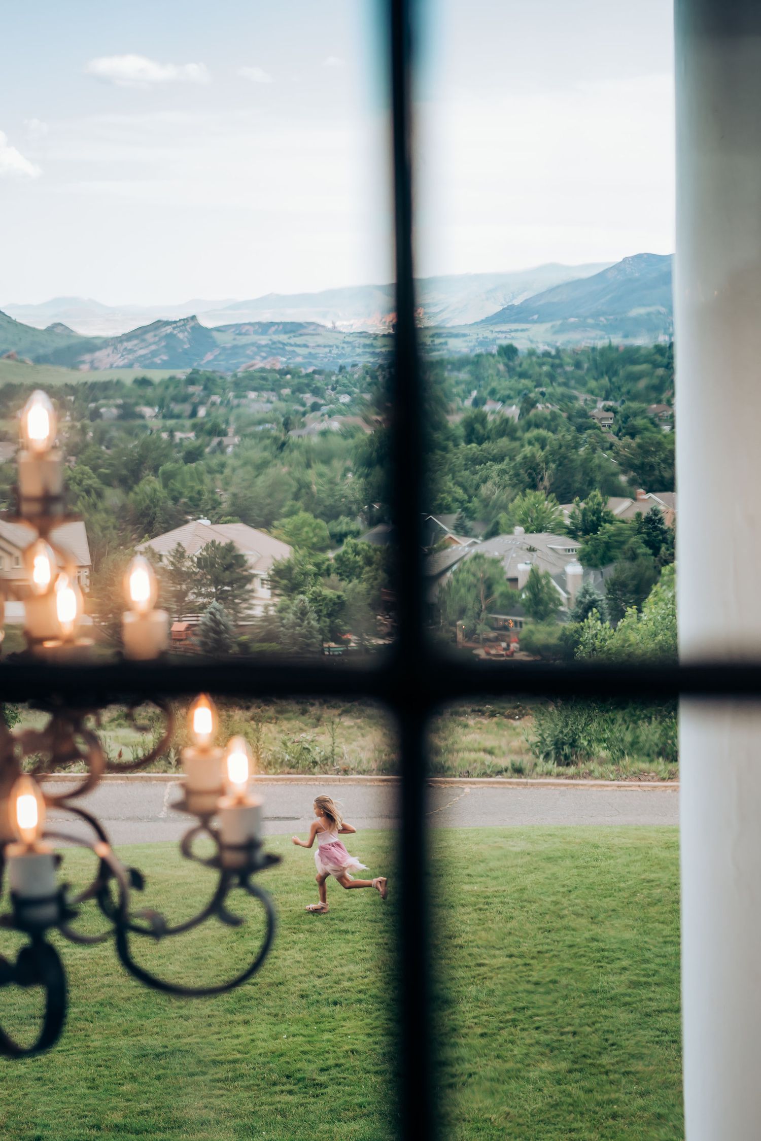 Candlelit view through window shows mountain landscape with green hills and a small figure running on grass below.