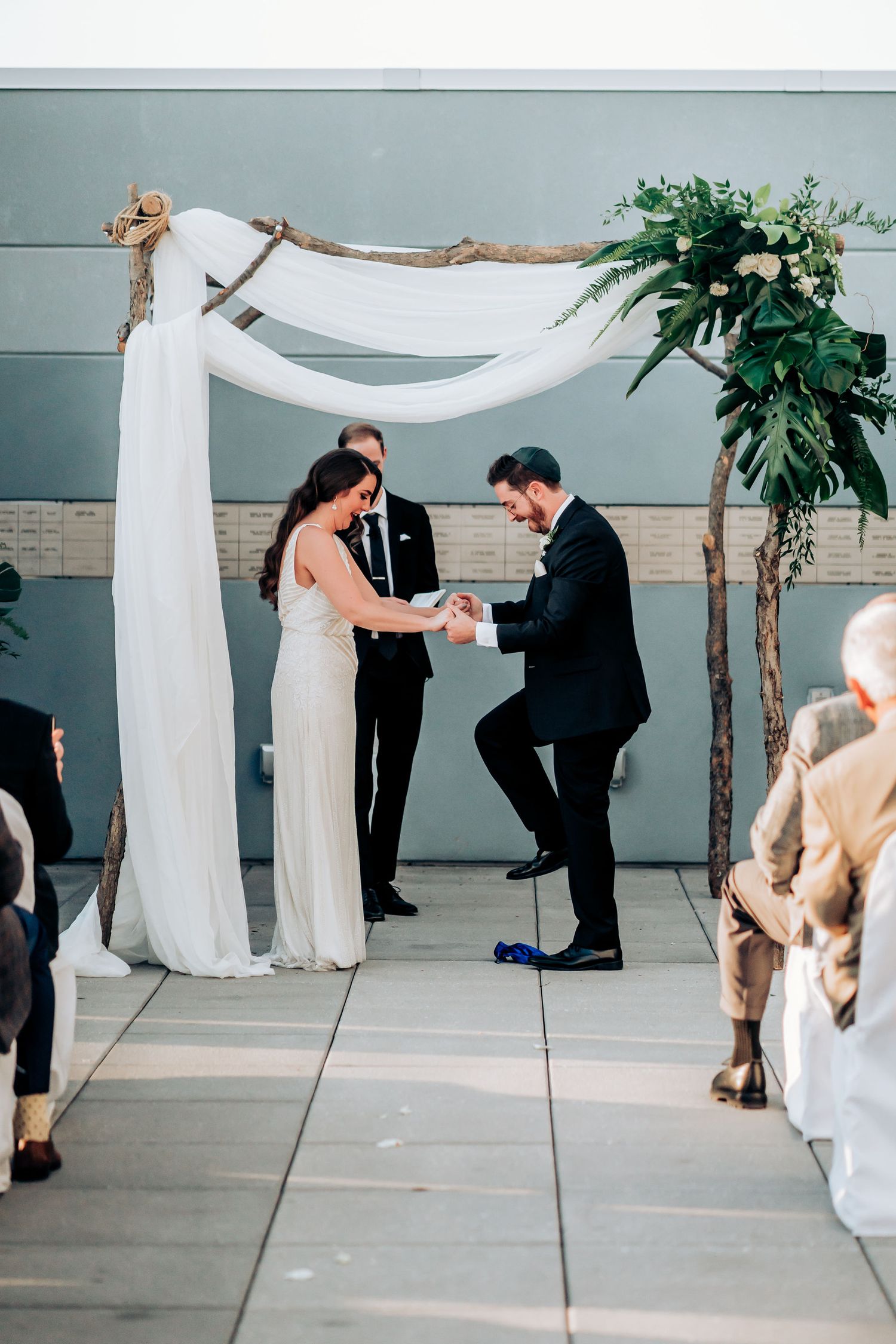 Intimate wedding ceremony moment under rustic arch with white fabric and botanical decorations.