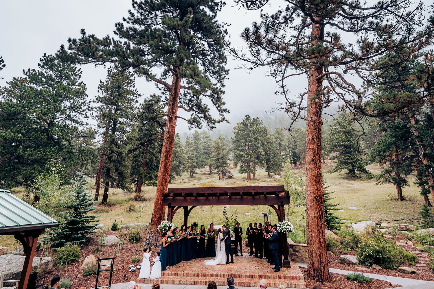 Rustic wooden pavilion nestled among tall pine trees during outdoor wedding ceremony.