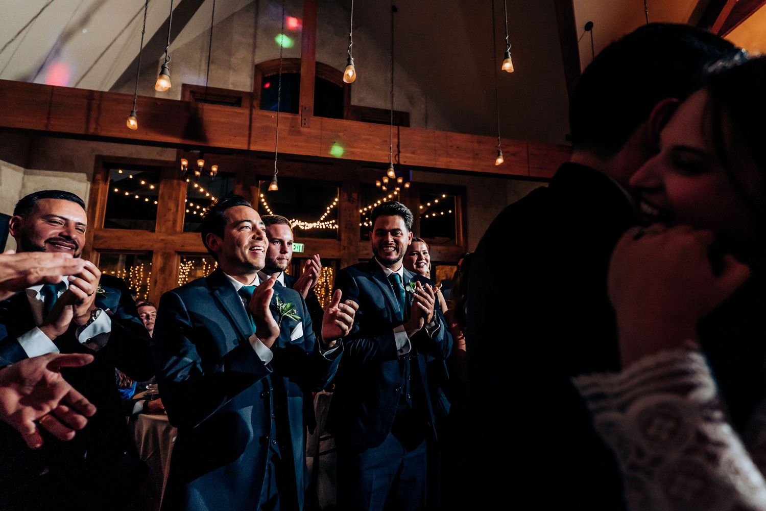 Wedding guests cheer and celebrate during a reception in a rustic wooden venue.