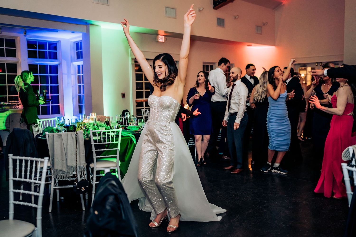A celebration with people dancing in a wedding venue with multicolored lighting effects.