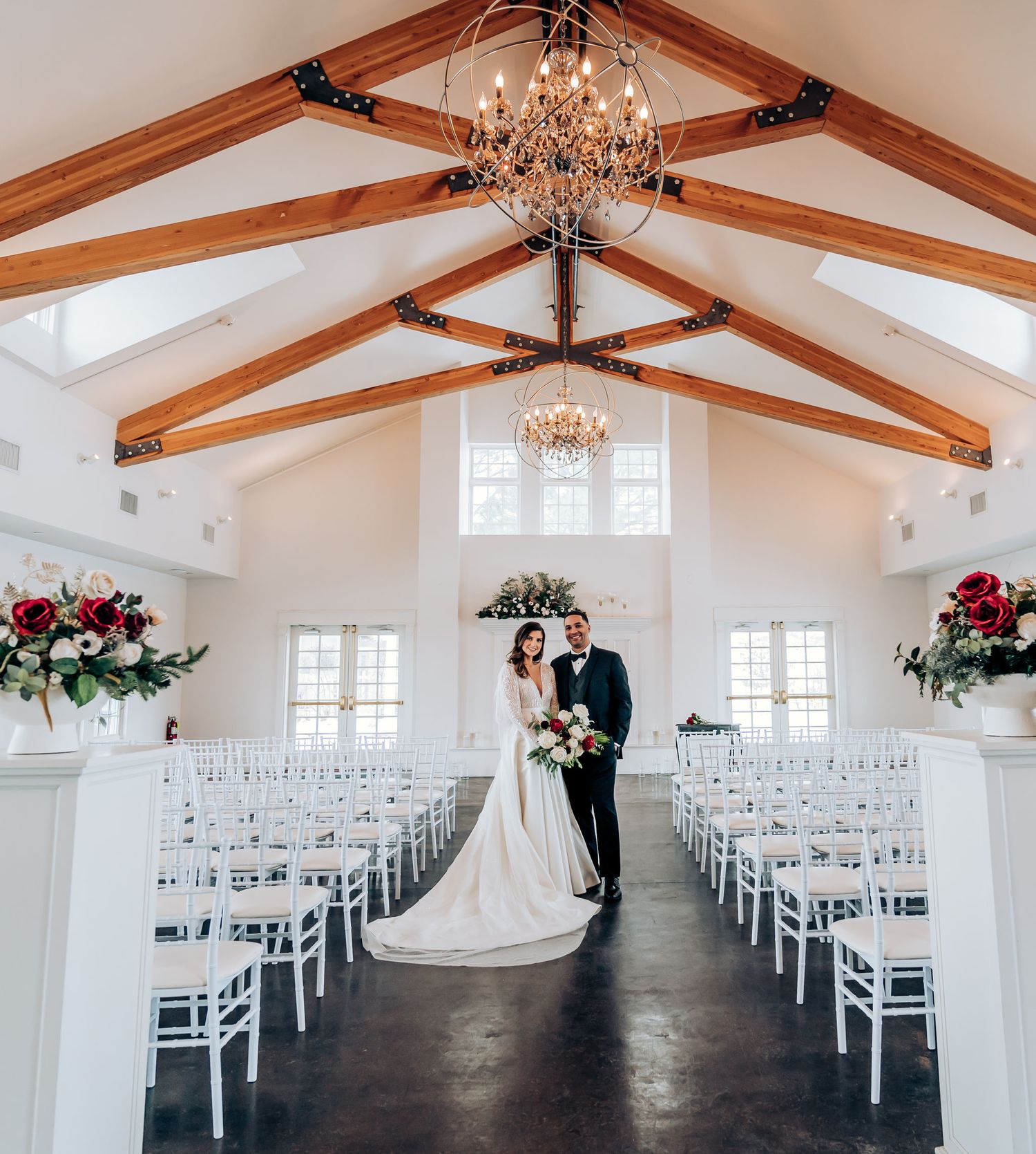 Chapel interior with vaulted wood beam ceiling, chandeliers and white chairs lined for ceremony.