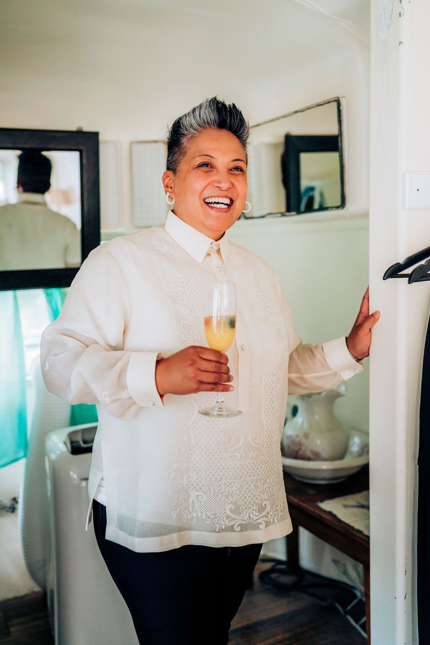 Person in traditional white barong holding champagne glass with joyful expression.