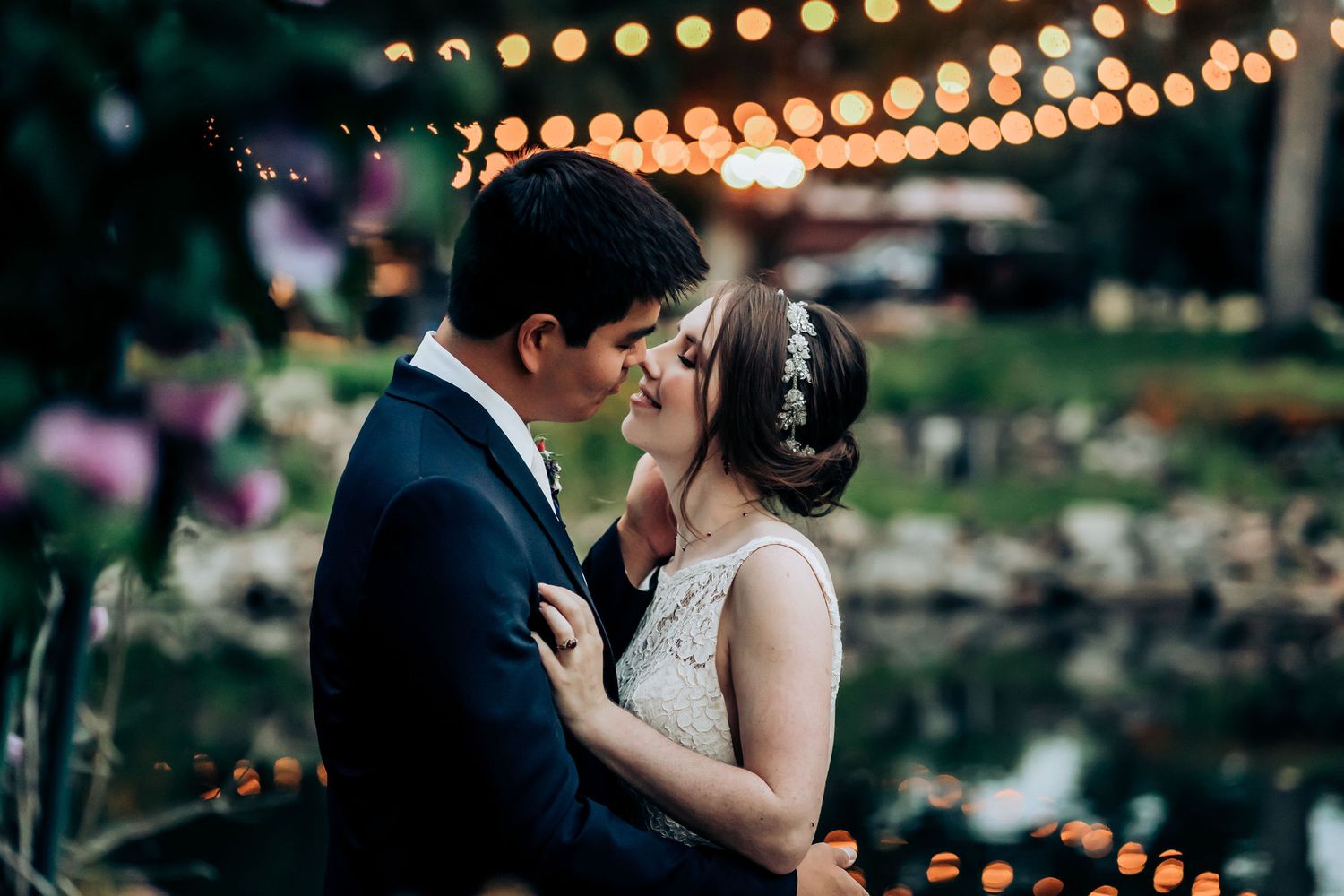 Romantic evening wedding portrait with twinkle lights glowing in the garden background.