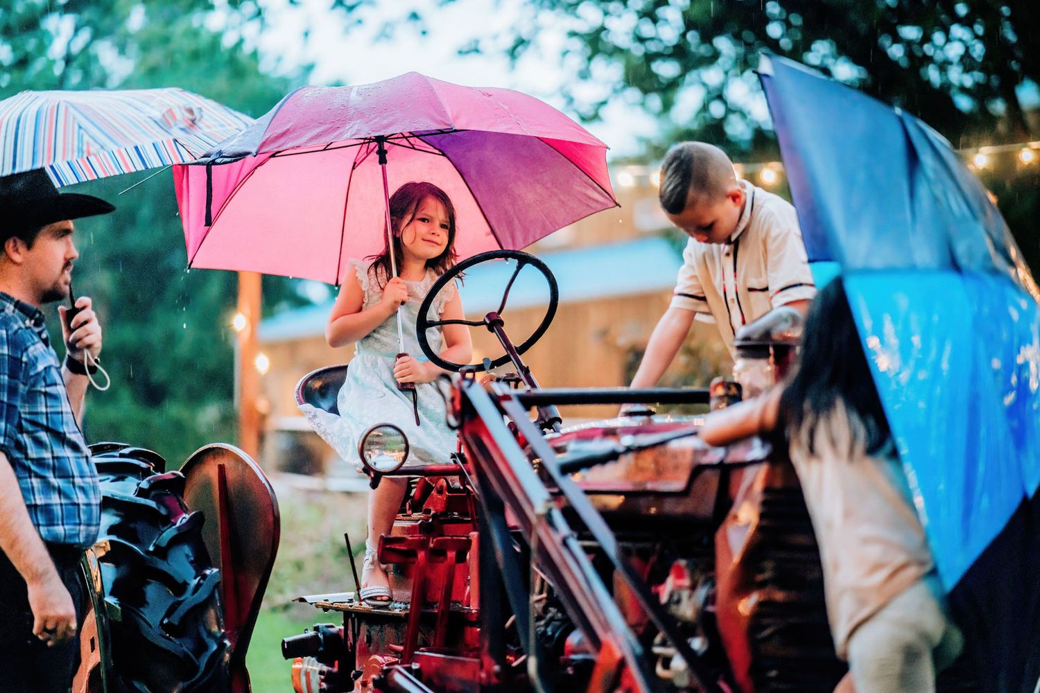 People examining vintage red tractor under colorful umbrellas on a rainy day.