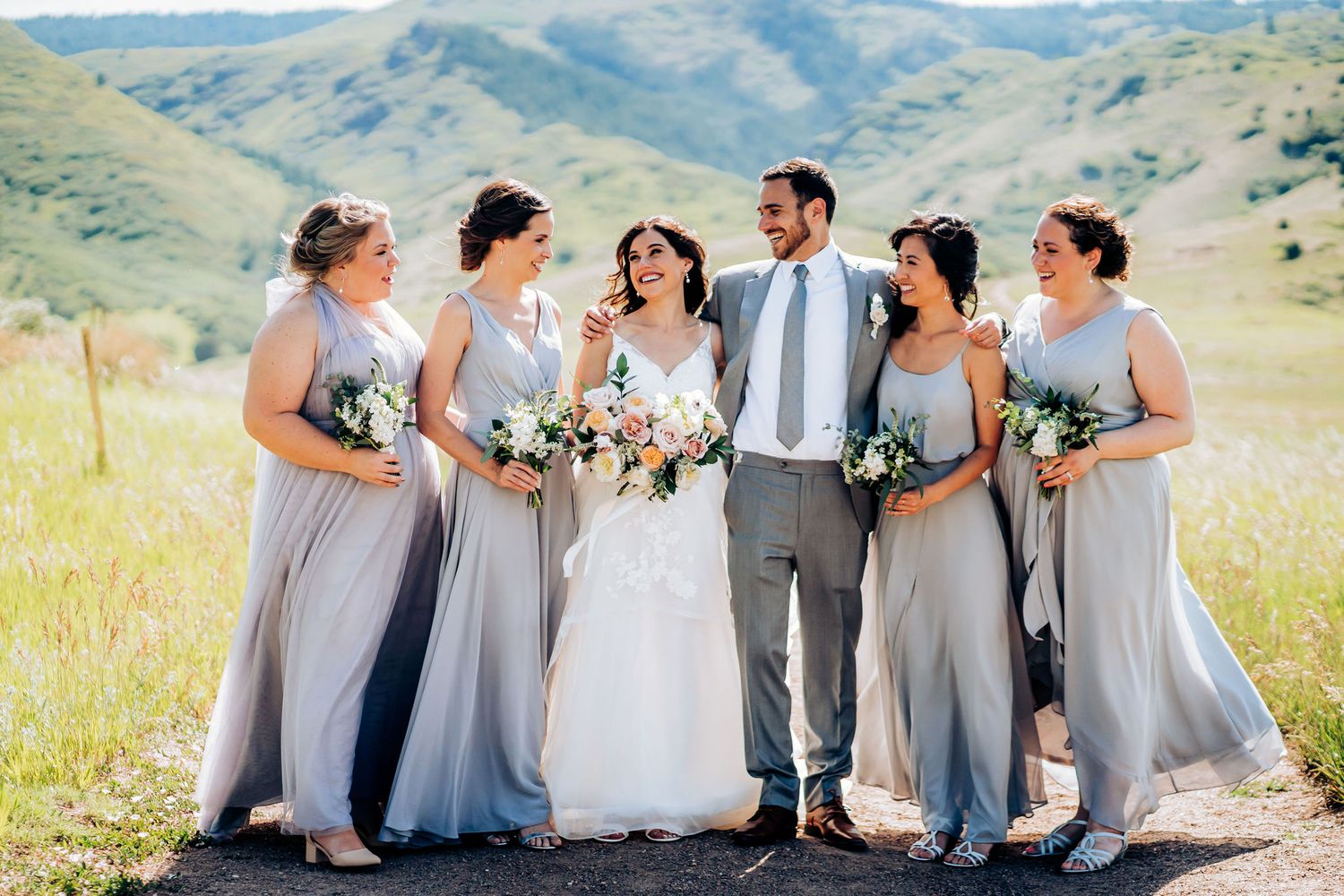 Wedding party in light gray dresses gathered on mountain path.