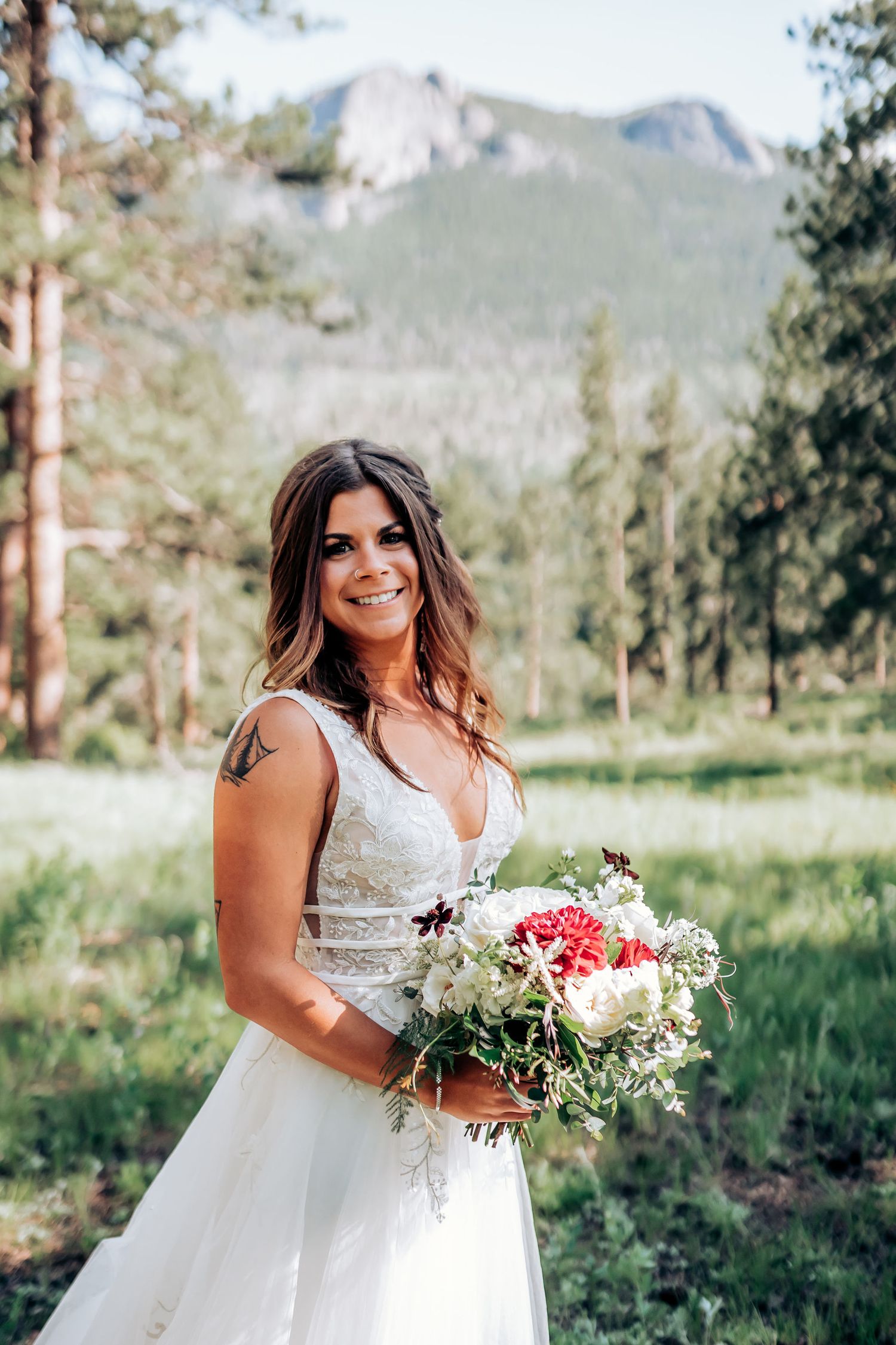 A stunning mountain wedding portrait showcasing a white gown and colorful bouquet against forest scenery.
