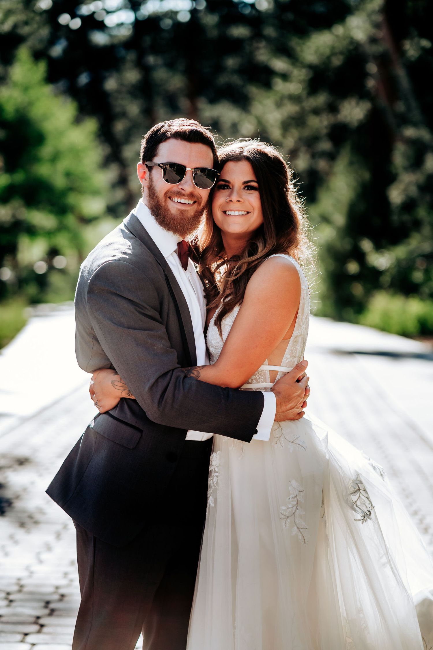 Happy couple embraces in sunlight on mountain pathway during wedding celebration.