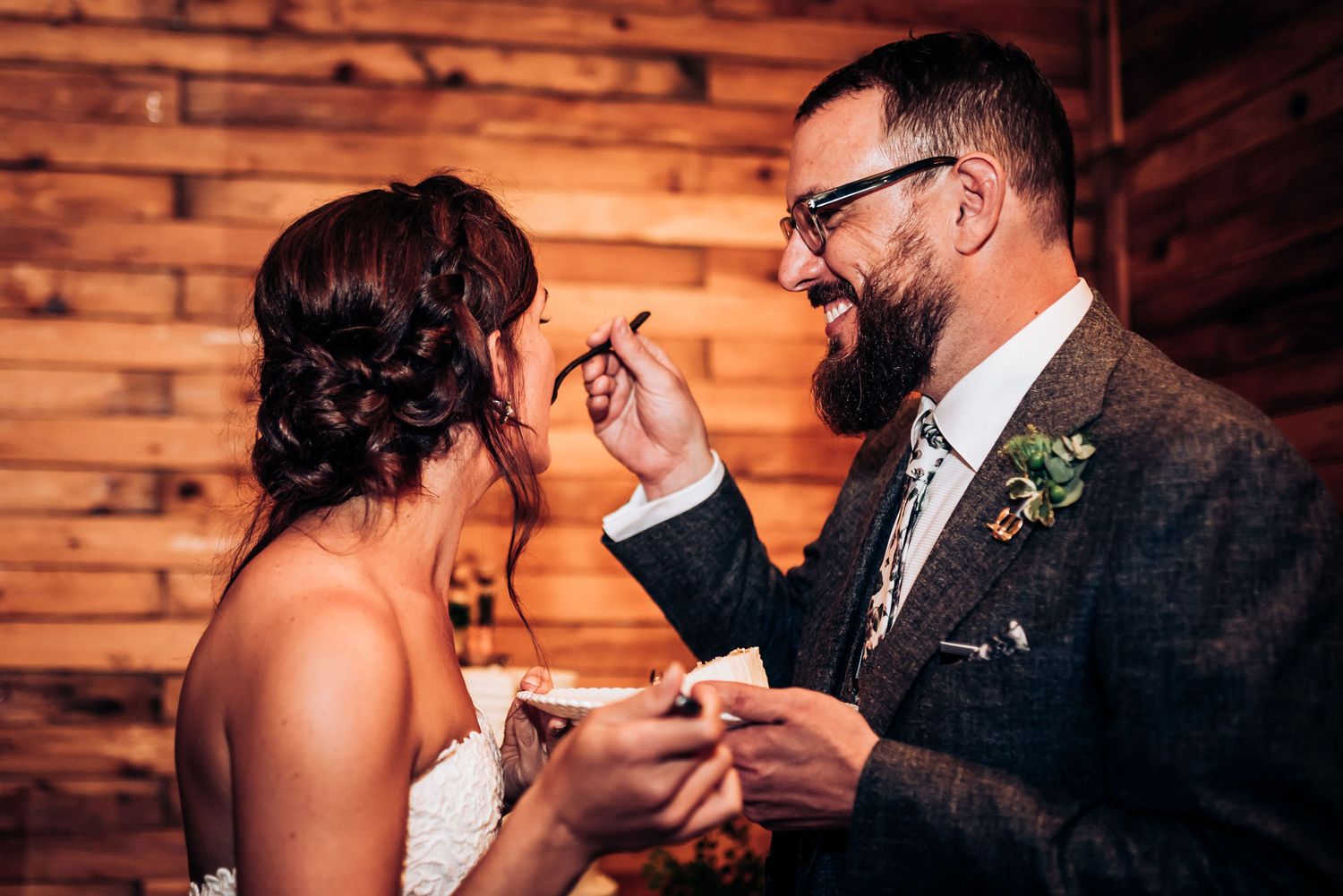 Couple sharing a joyful moment during cake cutting at rustic wedding reception.