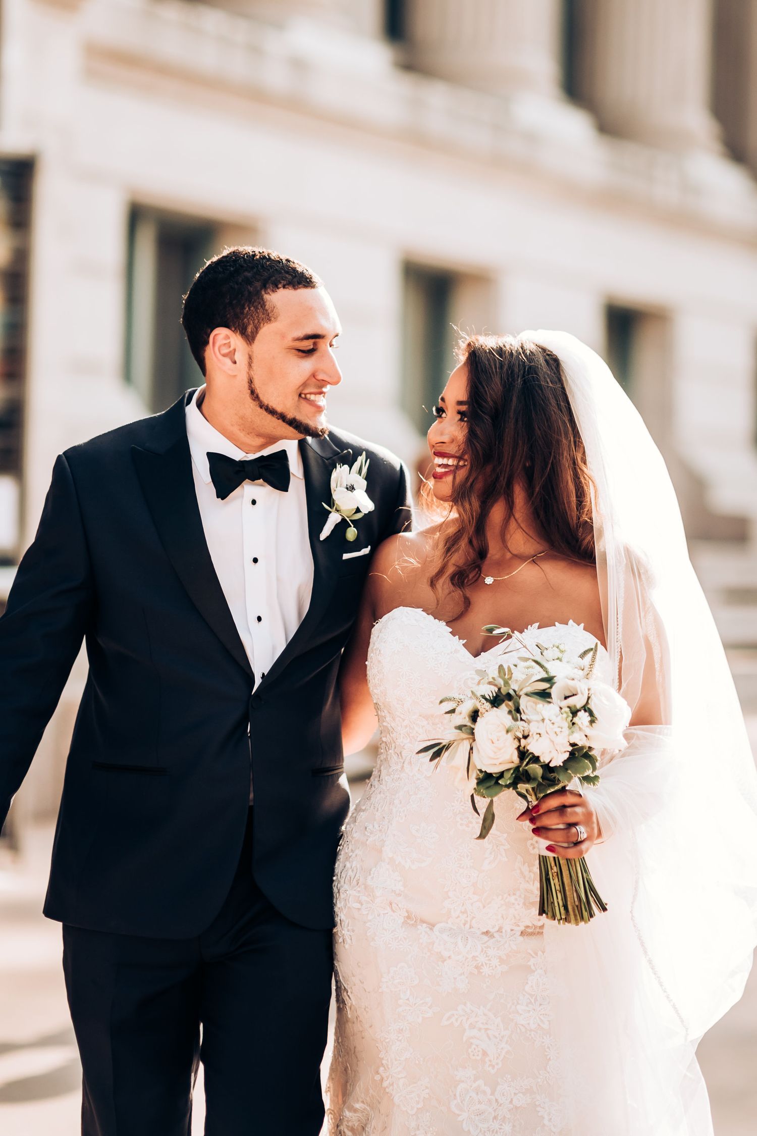 A joyful wedding couple shares a candid moment together while holding a white flower bouquet.