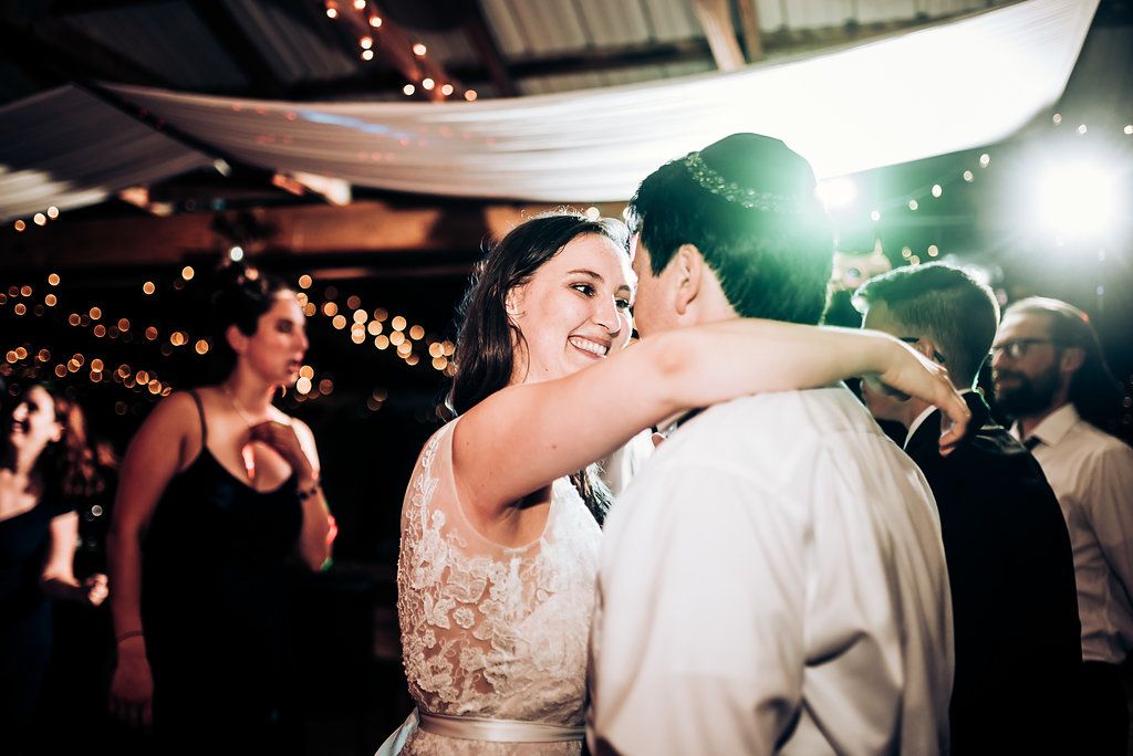 Dancing couples celebrate on the dance floor under romantic string lights at a wedding reception.