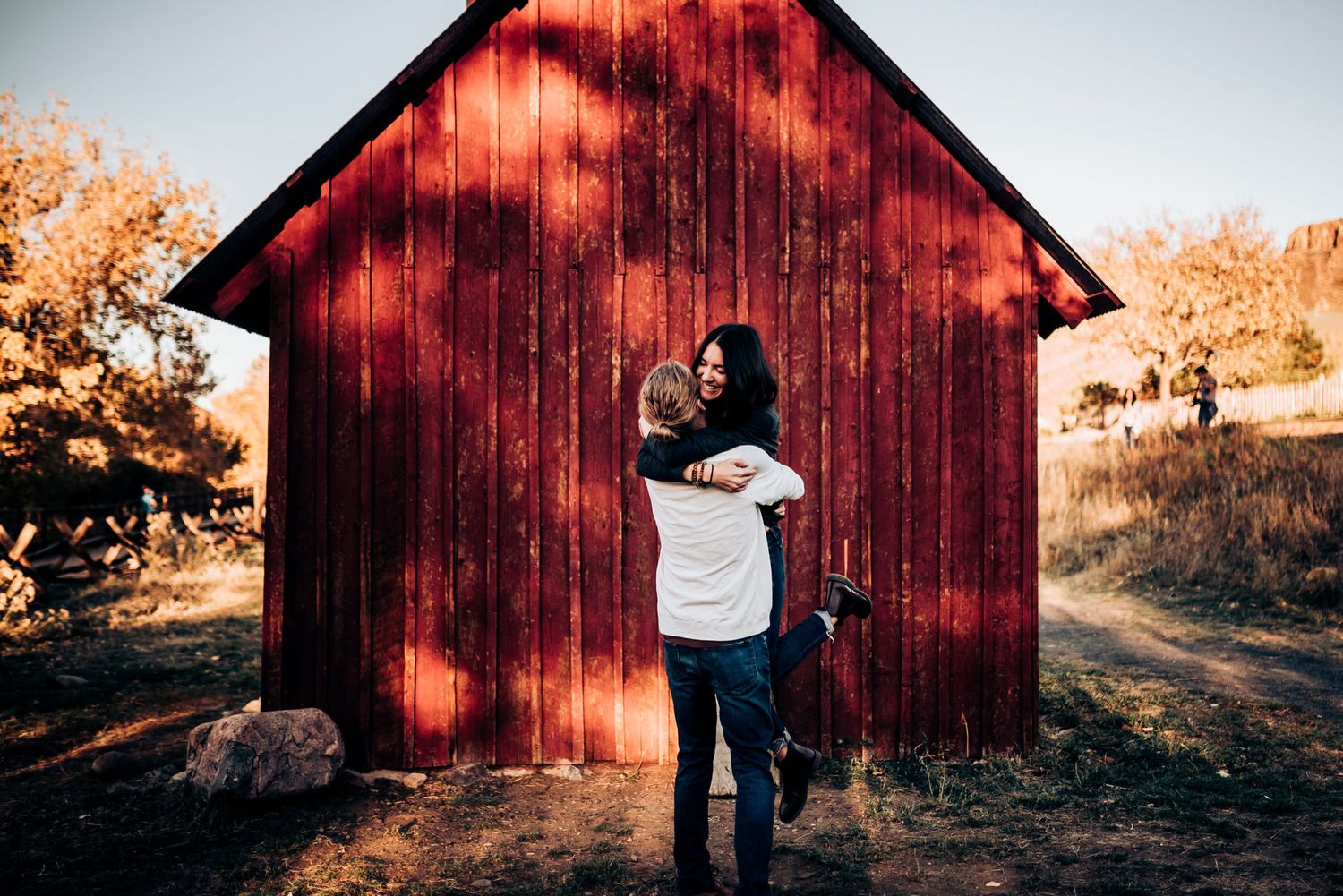 An intimate embrace captured in front of a weathered red barn during sunset.