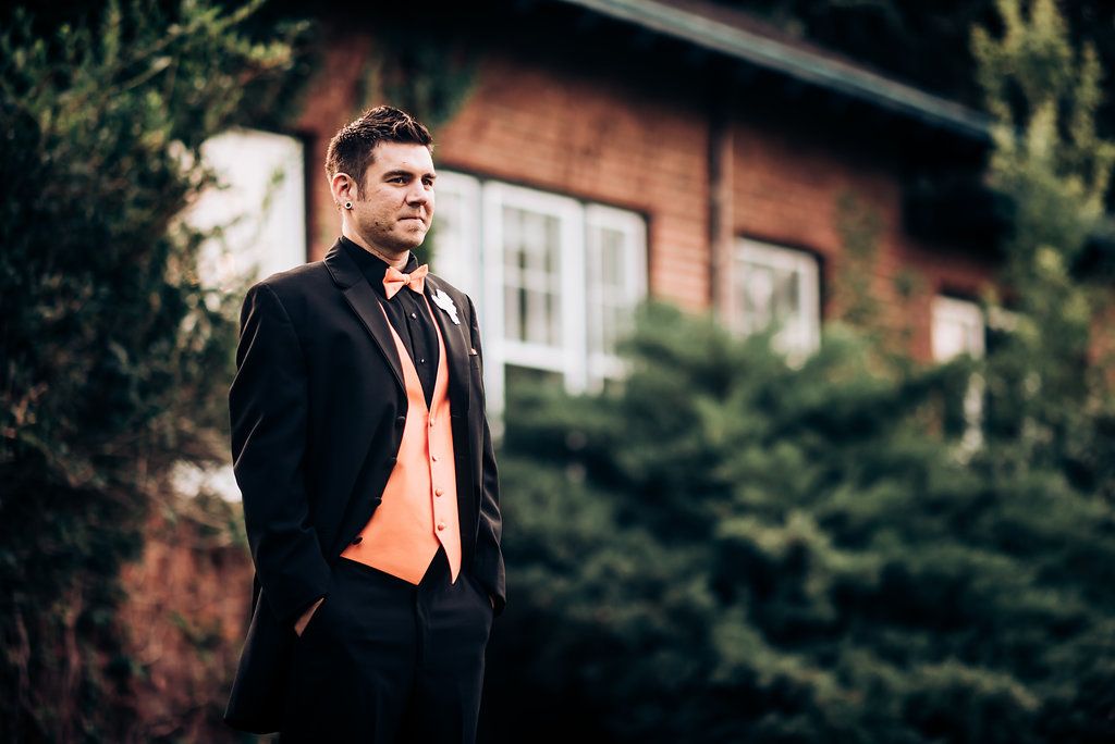 A formal portrait featuring black suit and orange vest against rustic outdoor backdrop.