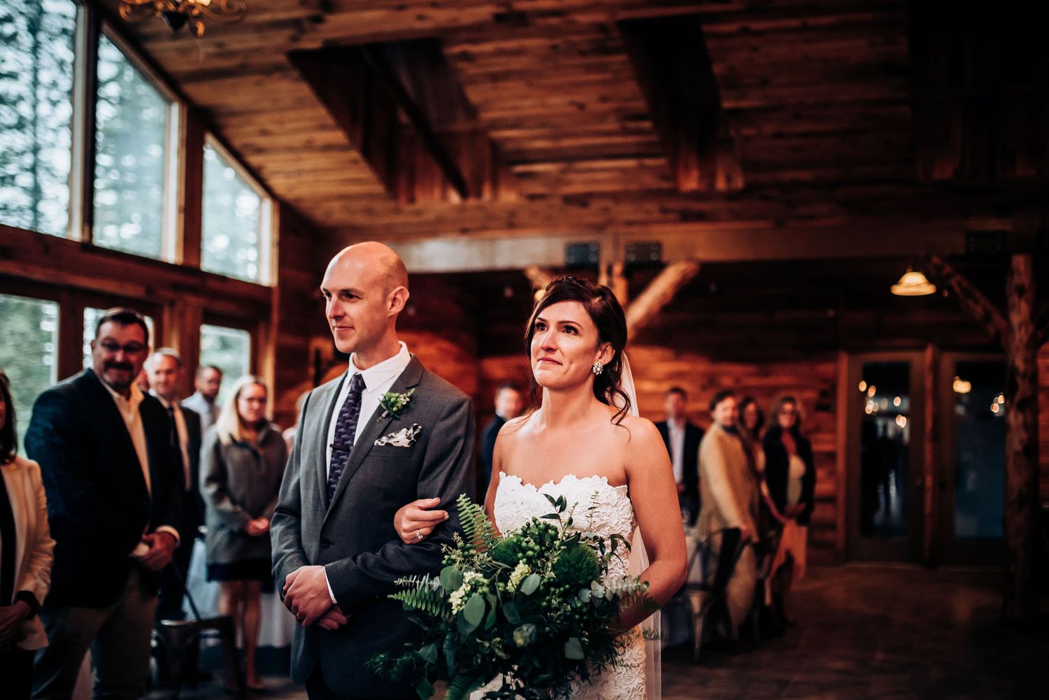 A couple stands at attention during their wedding ceremony in a wooden lodge.
