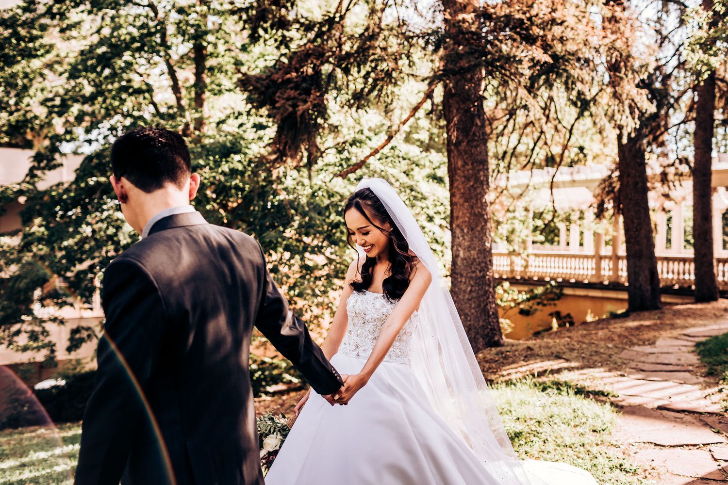 A tender wedding moment captured in a sunlit outdoor garden setting.