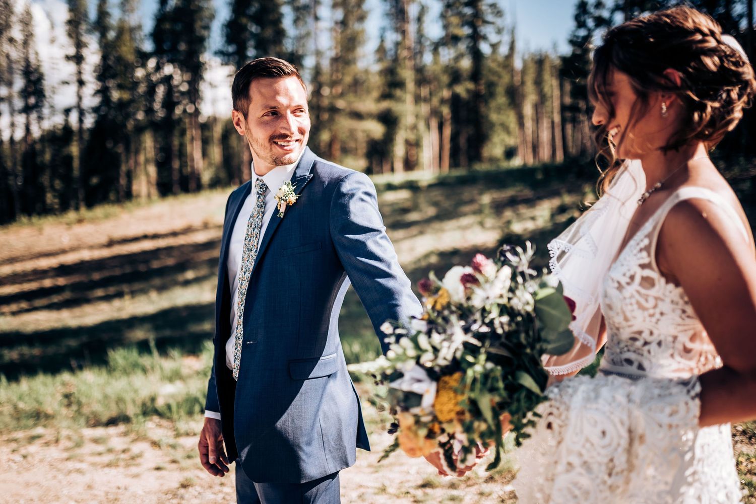 Wedding couple shares candid laughing moment outdoors with mountain scenery.