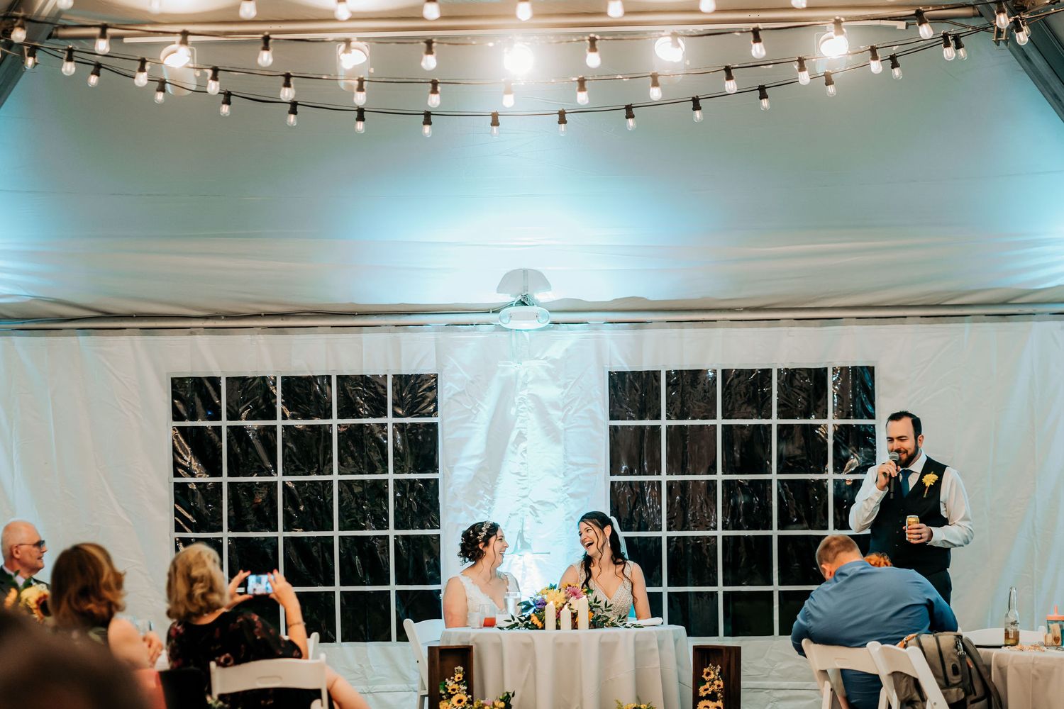 Wedding reception venue with string lights and guests seated at decorated tables.