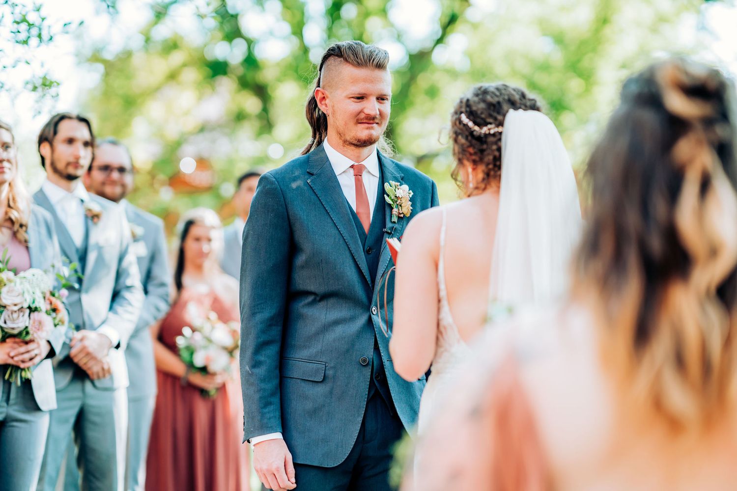 Wedding ceremony with attendants in teal and burgundy attire outdoors.