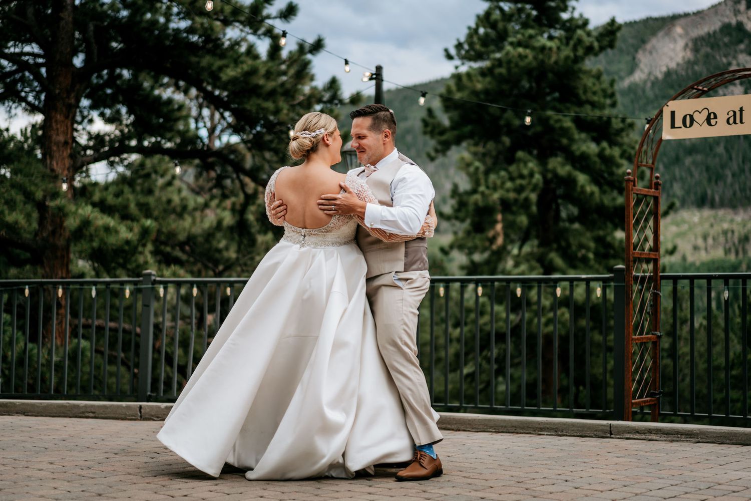 Couple dancing on outdoor terrace with mountain backdrop and pine trees.