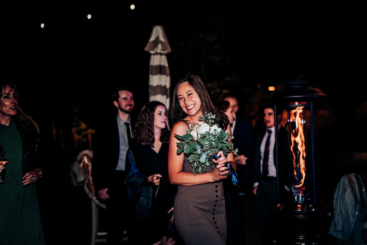 A person holding a bouquet of eucalyptus and white flowers at an evening event.
